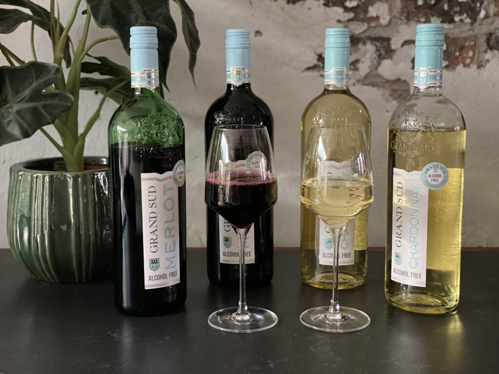 Twee glazen met Grand Sud alcoholvrije Merlot en Chardonnay naast de wijnflessen