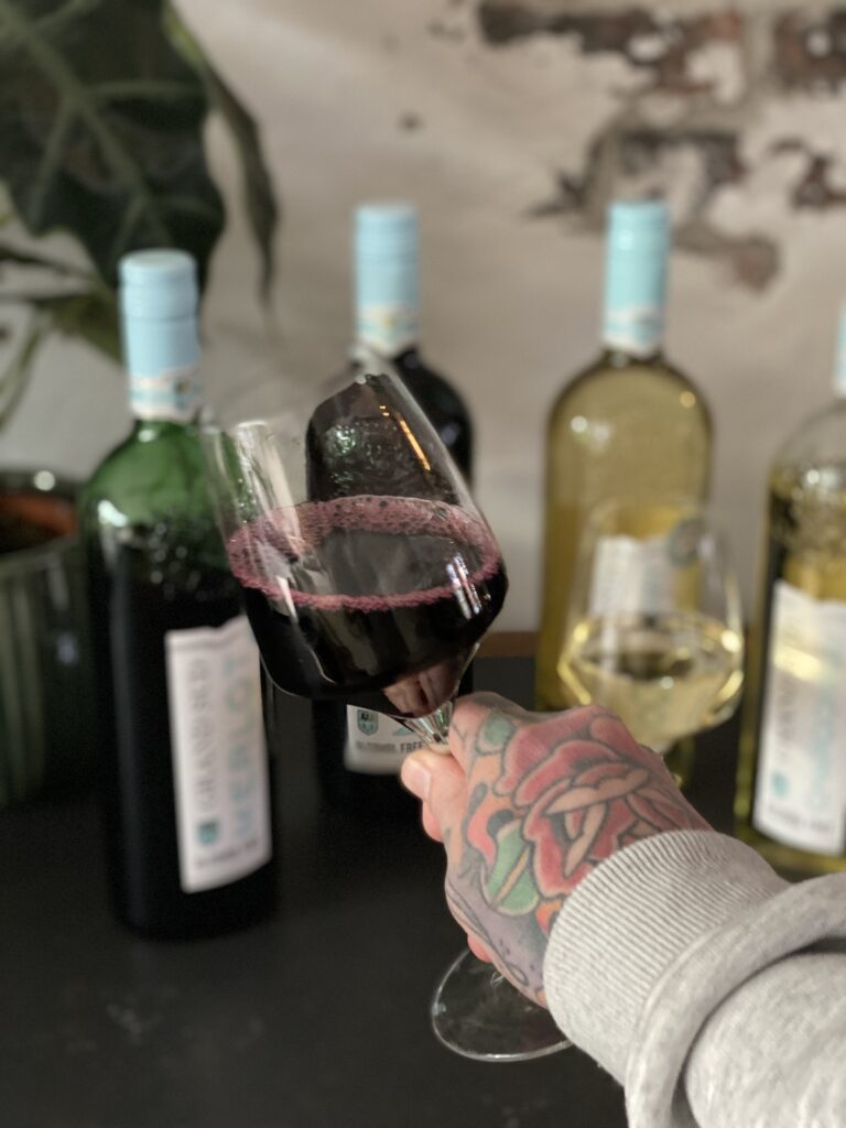 Hand met tattoo houdt een glas Grand Sud alcoholvrije Merlot vast