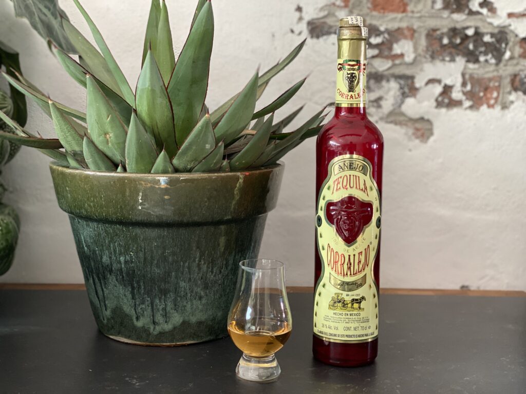 Een fles Corralejo Añejo tequila staat naast een agaveplant, de basis van deze ambachtelijke Mexicaanse tequila.